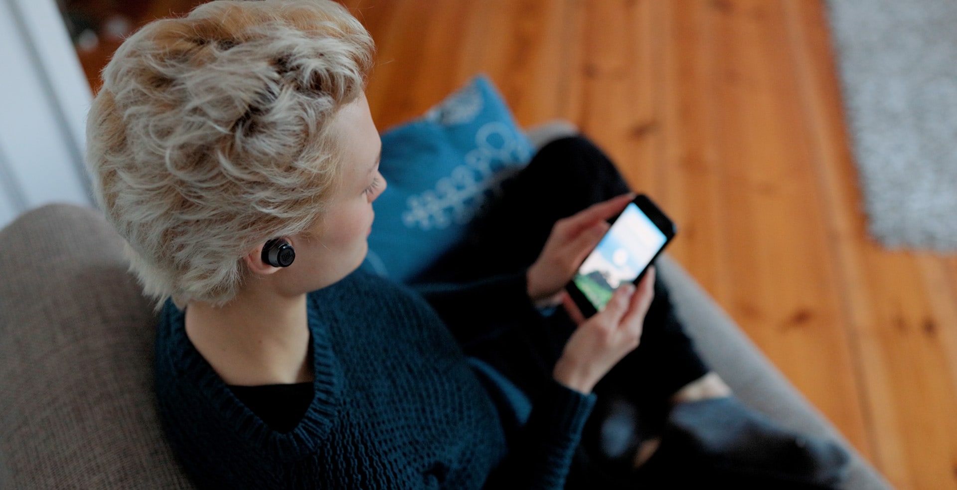A blonde woman with wireless earbuds in looking at her phone