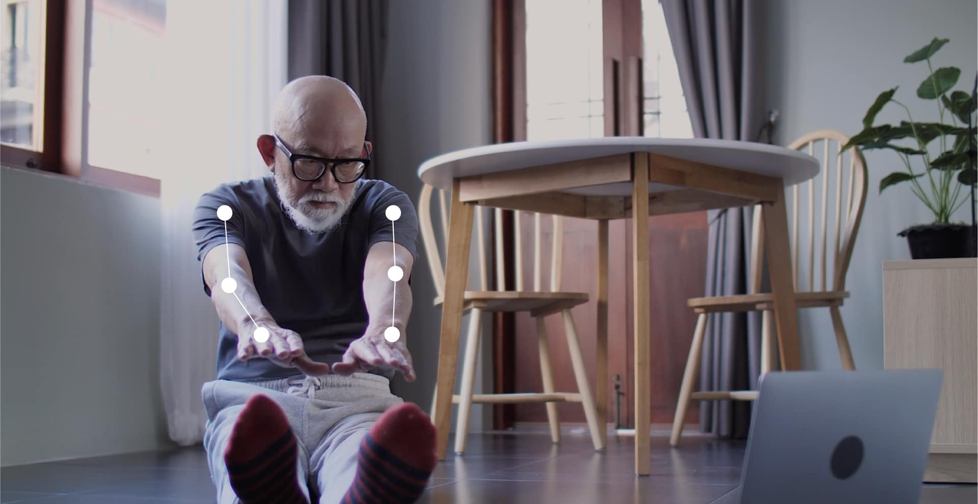 An old man sitting on the ground with his legs and arms straight in front of him stretching.