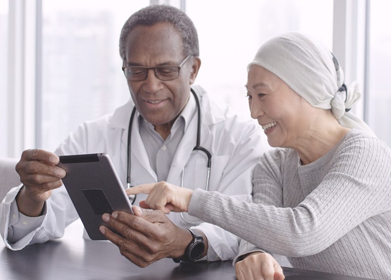 A male doctor holding an tablet with a woman who is a patient smiling and pointing to information on the tablet.